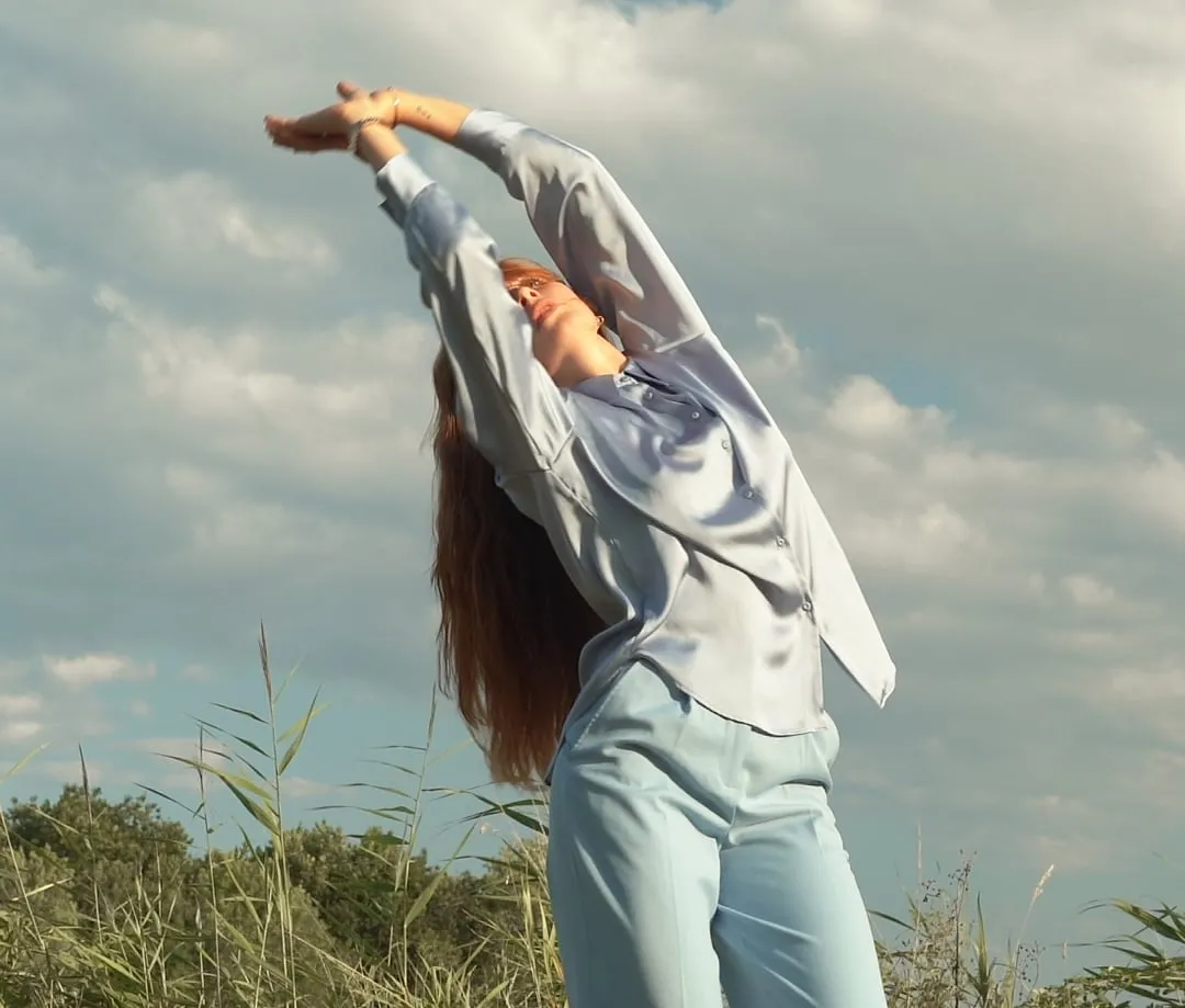 Danseuse qui lève les mains vers le ciel dans la nature