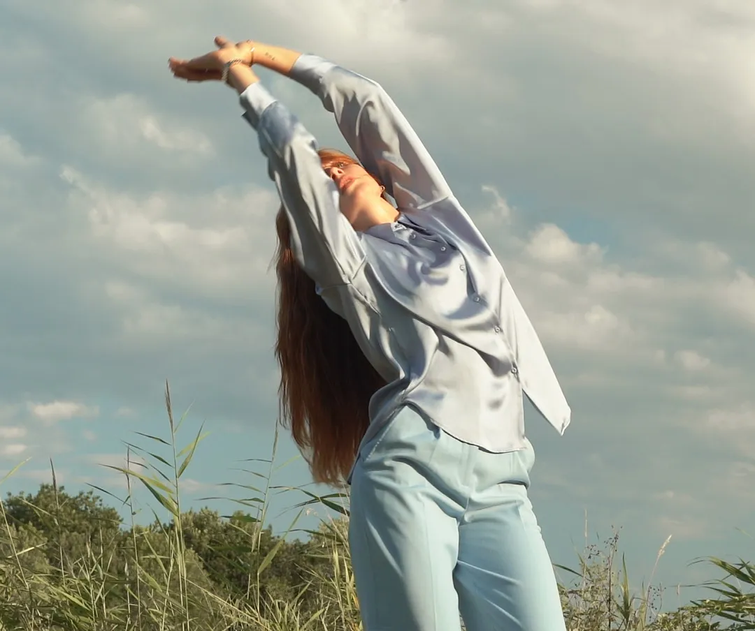 Danseuse qui lève les mains vers le ciel dans la nature