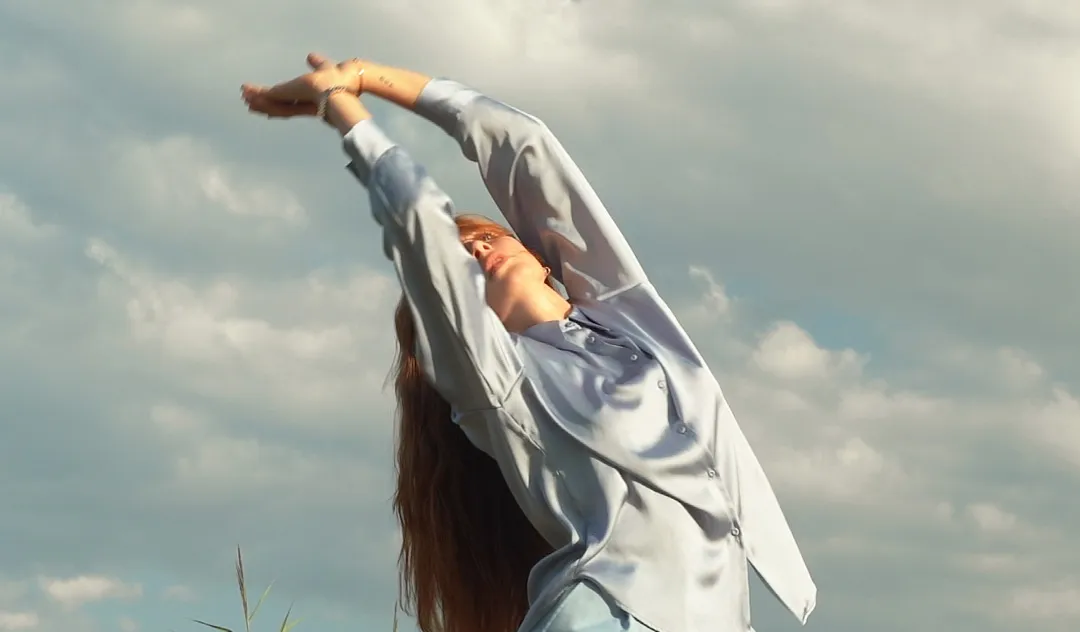 Danseuse qui lève les mains vers le ciel dans la nature